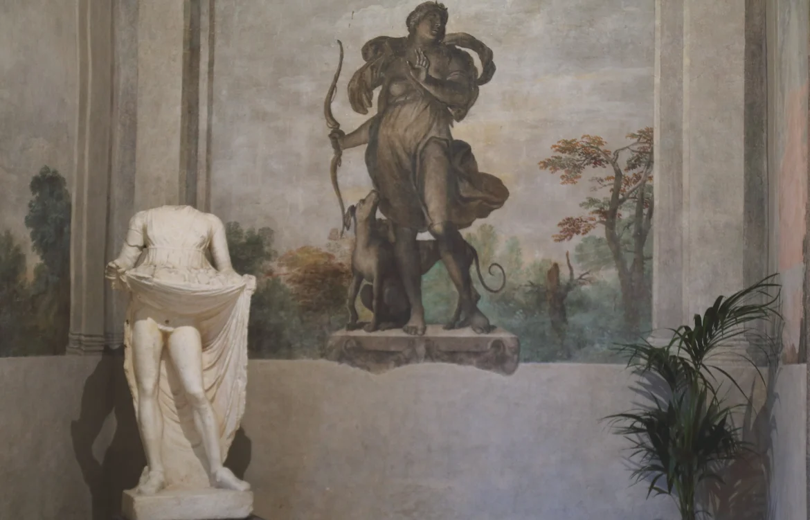 statua-di-maripara-bianca-senza-testa-in-una-sala-dipinta-alle-pareti-un-fauno-con-arco-e-levrieri